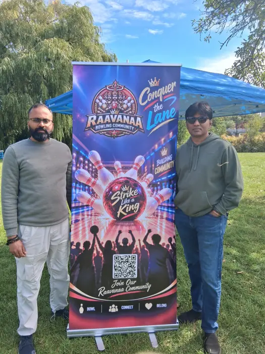 Two members standing beside the Raavanaa Bowling Community banner at an outdoor event