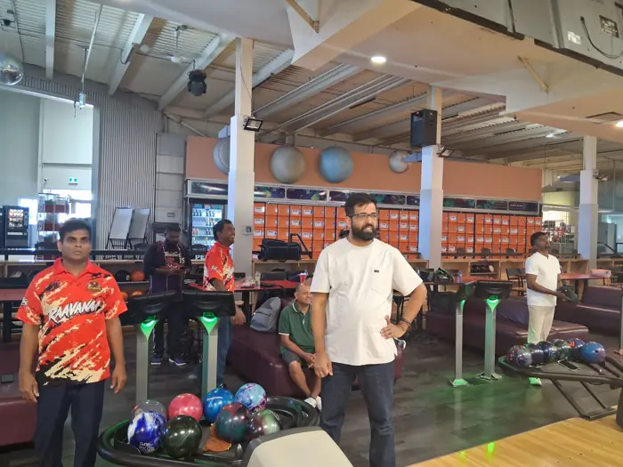 Members in orange Raavanaa jerseys standing at the lanes, watching a shot