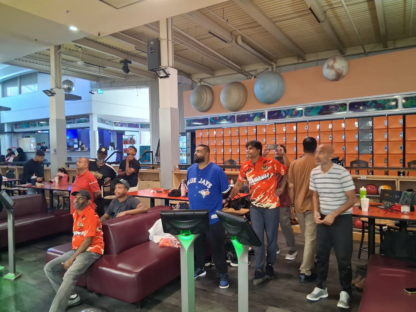 Club members, several in orange Raavanaa jerseys, watching the scores at the lanes
